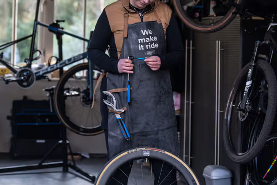 Somebody working in a bike workshop, wearing a apron with the text "We make ir ride"